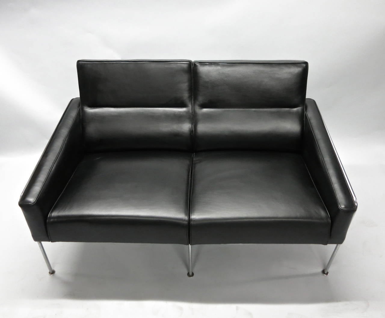 Vintage two-seat settee model 3302 designed by Arne Jacobsen and manufactured by Fritz Hansen for the Royal Hotel in Copenhagen. Newly upholstered in black leather and the metal frame is in excellent vintage condition.