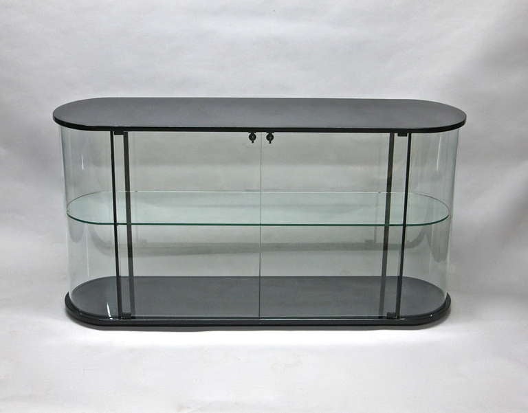 Display case with rounded clear glass at each end a clear contour shelf inside two doors each with its own lock no visible hinges top and bottom in black lacquered wood