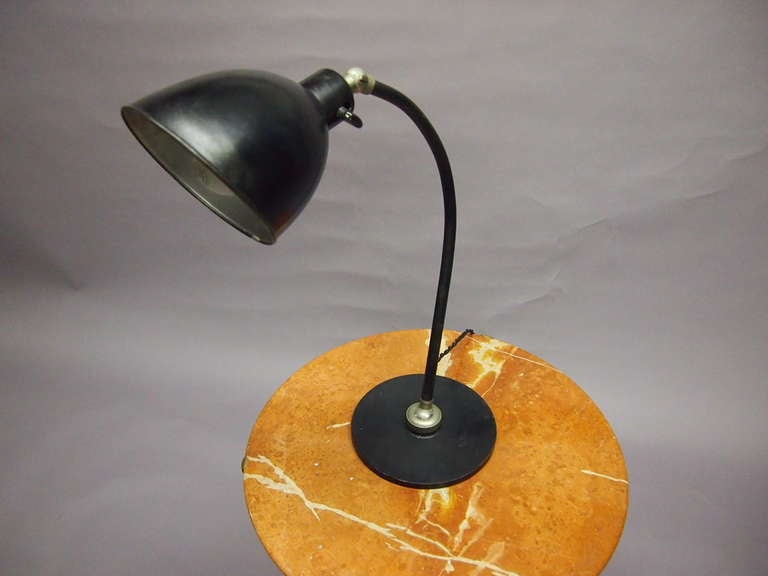 Table or desk lamp with a heavy, black enameled metal disc as the base that supports the body in the center with a metal joint that allows the lamp to move in all directions. The body is also black enameled metal but tubular and arched supporting