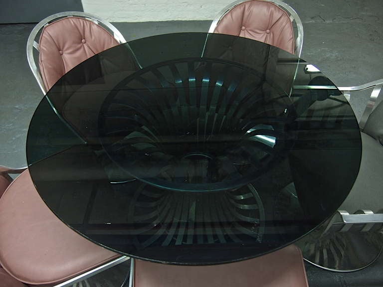 Dining Table with smoked glass top resting on an aluminum base surrounded by five swivel chairs one a captains chair.