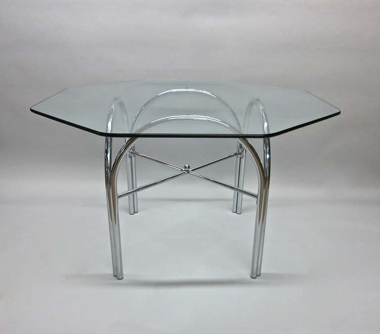 Garden or outdoor dining table in tubular polished steel shape in four arches held together with an x-shaped stretcher and a spherical finial in the center, all supporting an octagonal glass top.