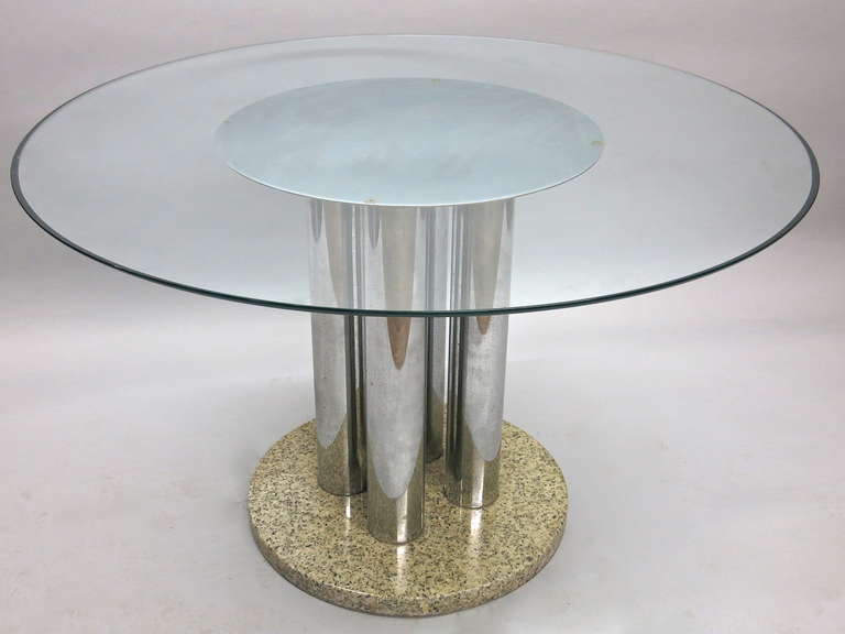 Dining Table has four metal columns with a stone base below and  polished metal above all supporting a round 3/4 inch glass top with rounded edges