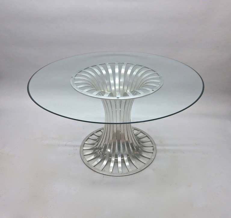 Dining table with round glass top and aluminum base made up of bands of metal splayed at the bottom and top meeting in the center to form a round column.
        ************FIVE CHAIRS  PART OF THE SET AVAILABLE**********