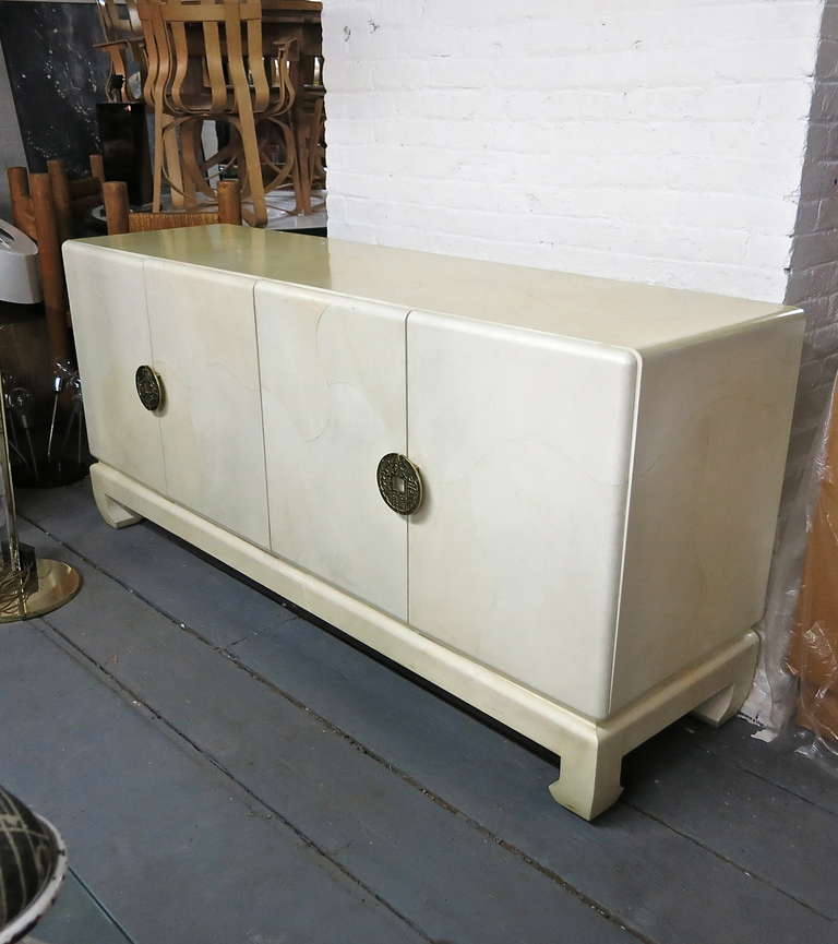 Sideboard in lacquered goatskin with four doors, nicely detailed brass pulls, and four arched feet supporting the platform and cabinet frame. The doors open to reveal drawers with shelves and two drawers that can compartmentalize objects,