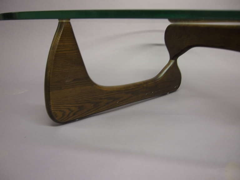 Low table with interlocking sections of wood that connect with a metal pin all supporting an original glass top 
designed by Isamu Noguchi for Herman Miller 1950's