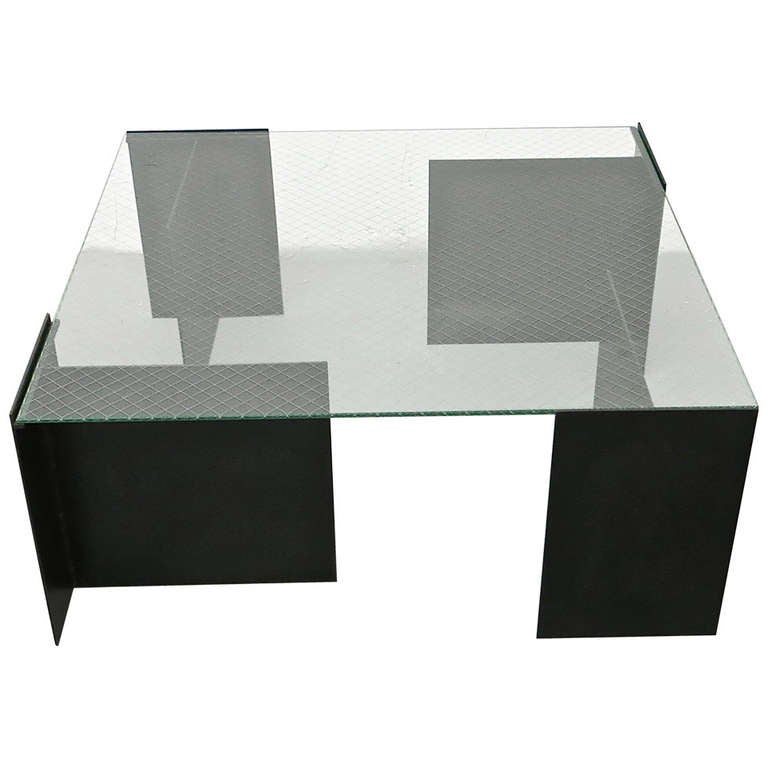 Coffee table with four T-shaped, solid steel legs and a clear safety glass top.