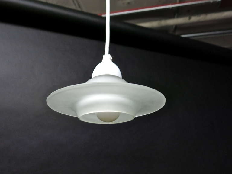 Small scale fixture saucer shaped in opaque glass shape attached to a white enameled metal diffuser that hides the wiring of the single candelabra socket. The light hangs from a single white wire that can be adjusted any length