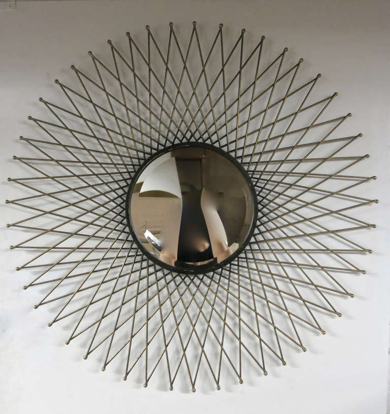 Wall mount beveled edge mirror set in a metal sunburst frame with a silvered, gilt, and black finish  throughout the metal frame