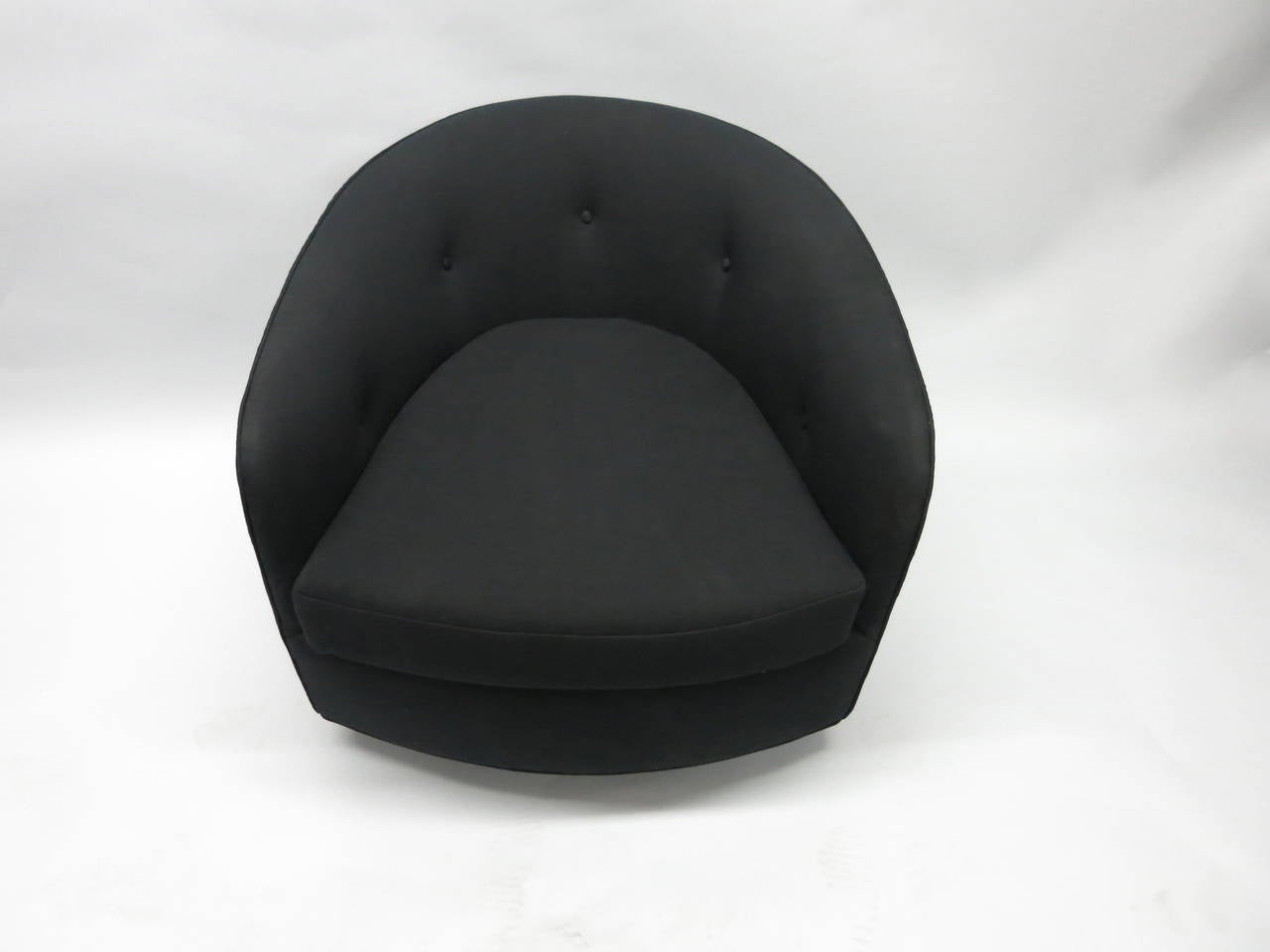 Pair of barrel back swivel chairs in newly upholstered black fabric. Each chair sits on a round wooden base that supports the metal fitting that allow the chair to rock, swivel and appear to float.