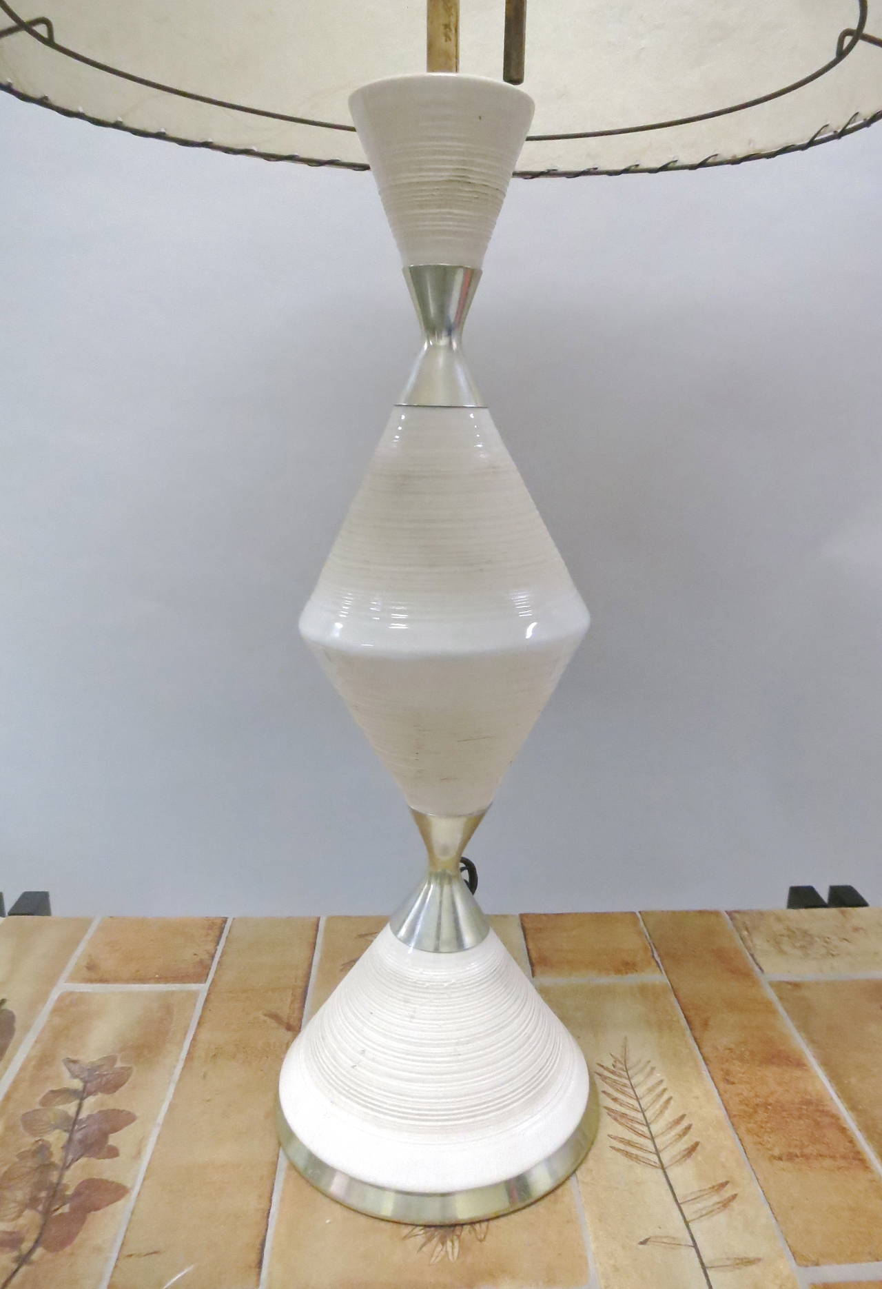 Table lamp has three levels of ceramic divided by polished brass with original shade in excellent vintage condition.