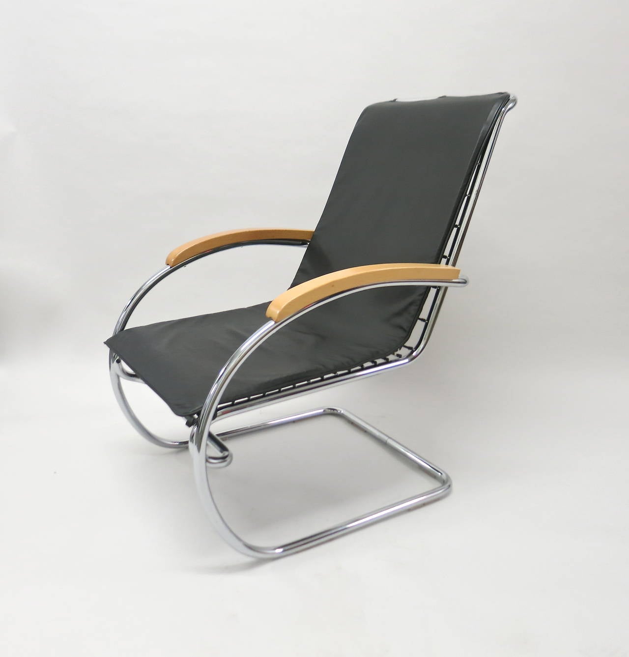 Pair of lounge chairs with chrome plated tubular steel frame, wood armrests and a single black leather cushion that attaches to the frame at top and bottom using leather ties sewn into the cushion. 
Anton Lorenz 1891-1964 originally designed the