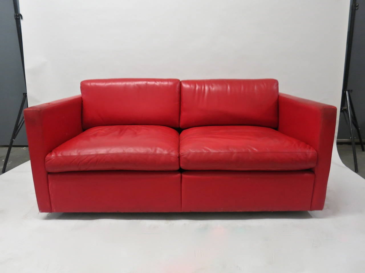 Two-seater sofa in original red leather. The original leather shows signs of wear but there are no rips. The sofa has six black enameled solid steel supports that float the sofa 2 inches off of the floor. Needs a good cleaning but will last another