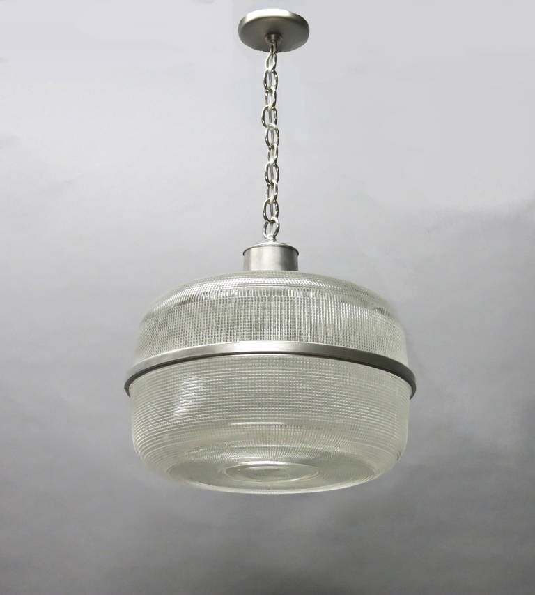 Ceiling fixtures in holophane glass, a brushed aluminum center band, and a steel housing that have been rewired with a standard American porcelain socket. A removable glass disc at the bottom allows easy access to bulbs.
