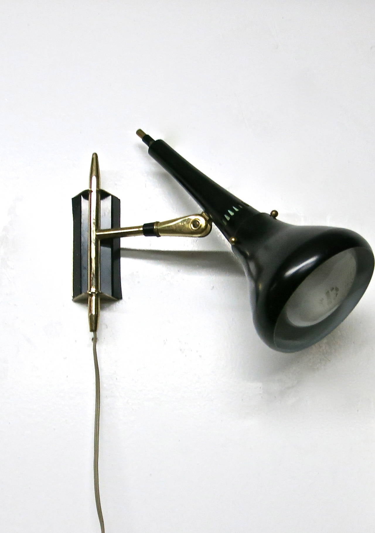 Pair of functional and well made articulating wall mounted light fixtures in brass and metal, enameled black on the outside of the shade and enameled white on the inside. The brass arm moves the shade and arm from left to right, and the black shade