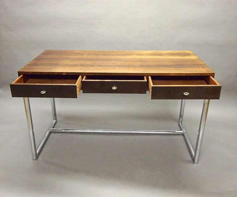 Rosewood Desk with three equal drawer each having a solid steel ring pull. The top is supported by a tubular chrome rectangular base at each end that are connected at the bottom by a chrome stretcher.