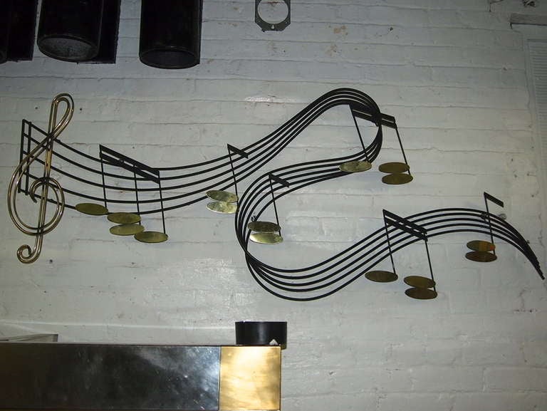 Wall sculpture in enameled metal with brass musical notes the brass is consistent in color the lighting causing shadows make them appear to be different shades signed and dated