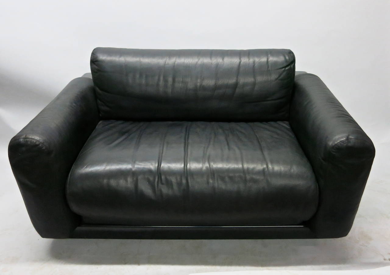 Black leather loveseat with a molded plastic frame with a molded notch for storage in the back.