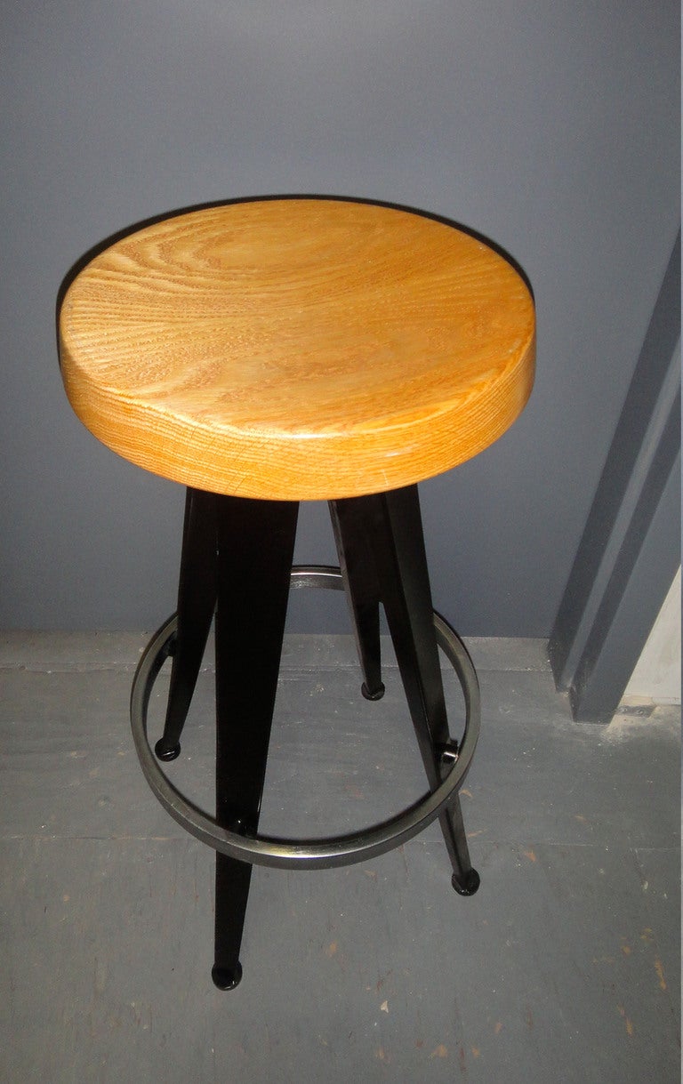 10 Stools with a round wood seat supported by four splayed legs in black enameled steel and an aluminum foot rest. Styled in the manner Jean Prouve