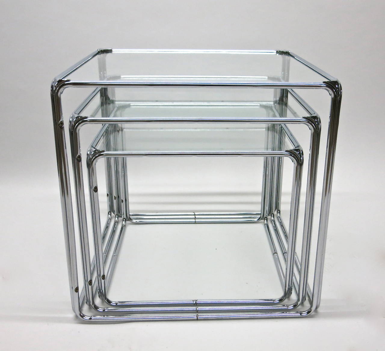 Three stacking tables all cubes with chrome-plated tubular steel frames. Each corner has a triangle joint that connects the frame and covers the fittings. All three tables have a glass top and stack small to large over the top.