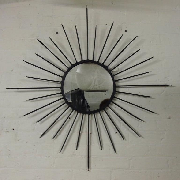 A twelve inch round mirror at the center of this starburst, wall decor comprised of 32 hand hammered wrought iron rods.