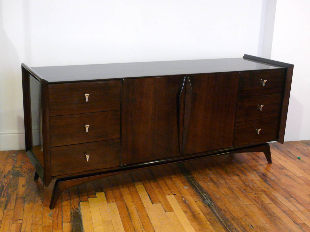 Exceptional Mid-Century credenza in the manner of Gio Ponti with beautiful flared ends resting on a sculptural base.  The middle doors reveal 3 additional deep drawers for extra storage space. Perfectly refinished in a high gloss medium walnut with