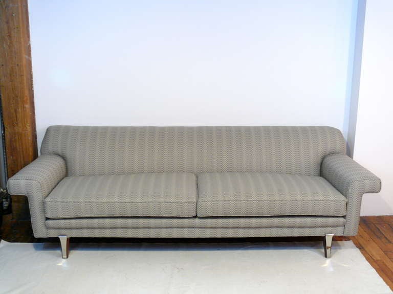 Very unique Mid-Century two cushion sofa with wide cantilevered arms and tight back. The crowning jewels of this sofa are the tapered walnut legs which have nickel scrolled appliques.