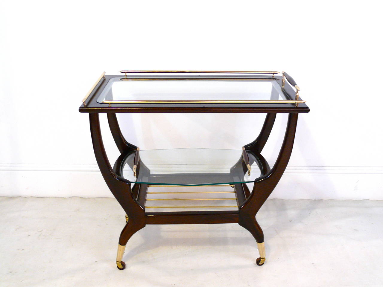 Fantastic three-tier bar cart in the manner of Gio Ponti with beautiful brass accents and casters. It has a top glass tier with brass stretchers, a middle glass removable tray with handles and a brass rod third tier. Refinished in a gorgeous