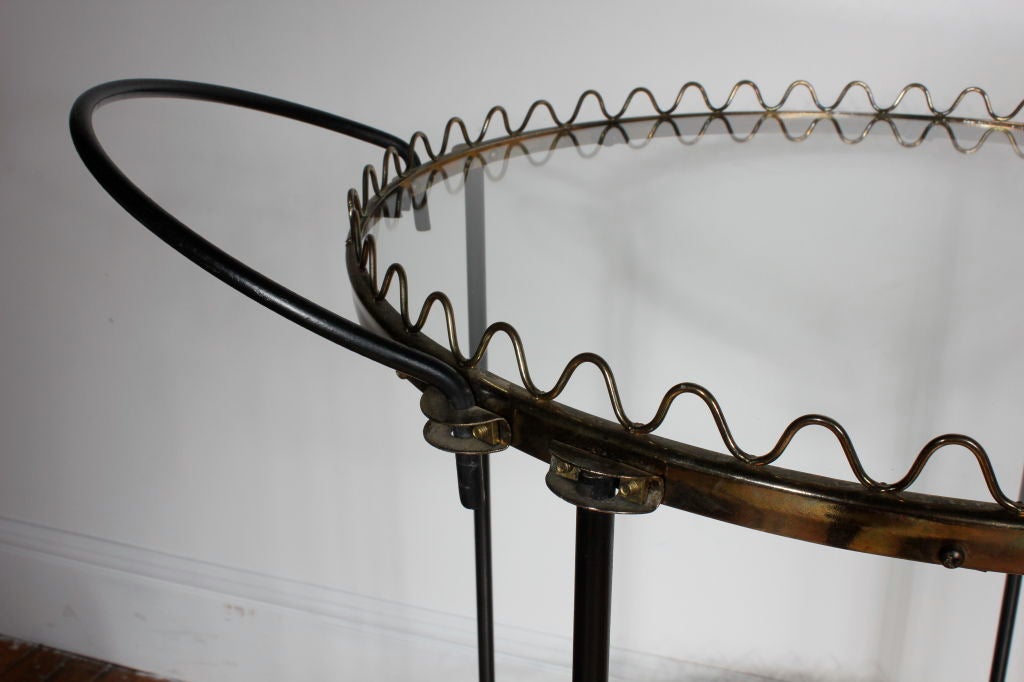 Jean Royere influenced scalloped two tier brass, iron and brass bar cart   Each tier is trimmed in a brass scallop and has inset glass.  The iron frame is spared no detail with a beautifully brass trimmed center support. There are four wheels for