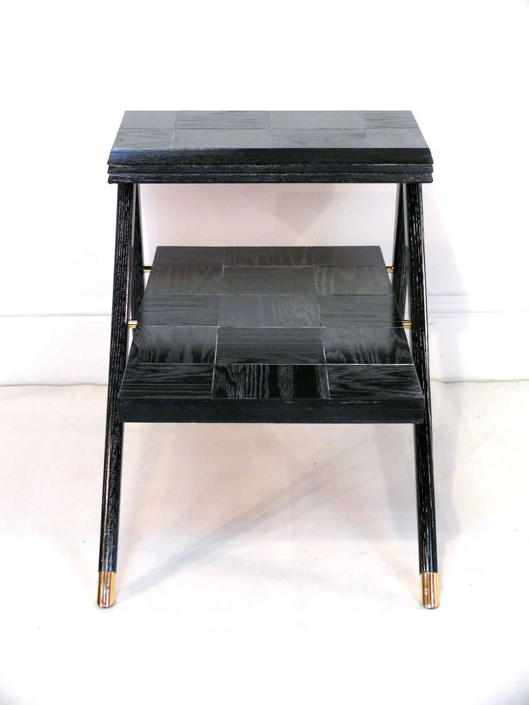 Elegant pair of tiered end tables in the style of Gio Pontii. The tops have a parquet effect and the black cerused finish is accentuated by brass sabots and hardware.