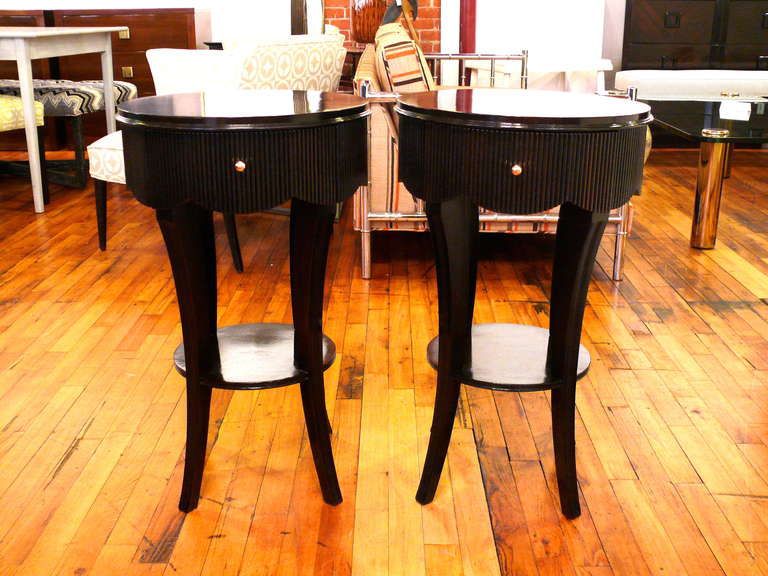 Elegant pair of two-tiered round side tables with a scalloped reeded skirt and lower shelf in the manner of Grosfeld House. The tables have one drawer with a small brass pull. The tables have been refinished in a deep espresso over walnut.