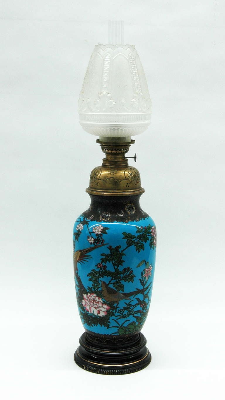 A 19th century Japanese cloisonné enamel vase with an oil-burning lamp fittings. The body of the lamp is decorated with painted images of birds and foliage, and the tank, burner, and glass shade resemble the theme with intricate floral designs by