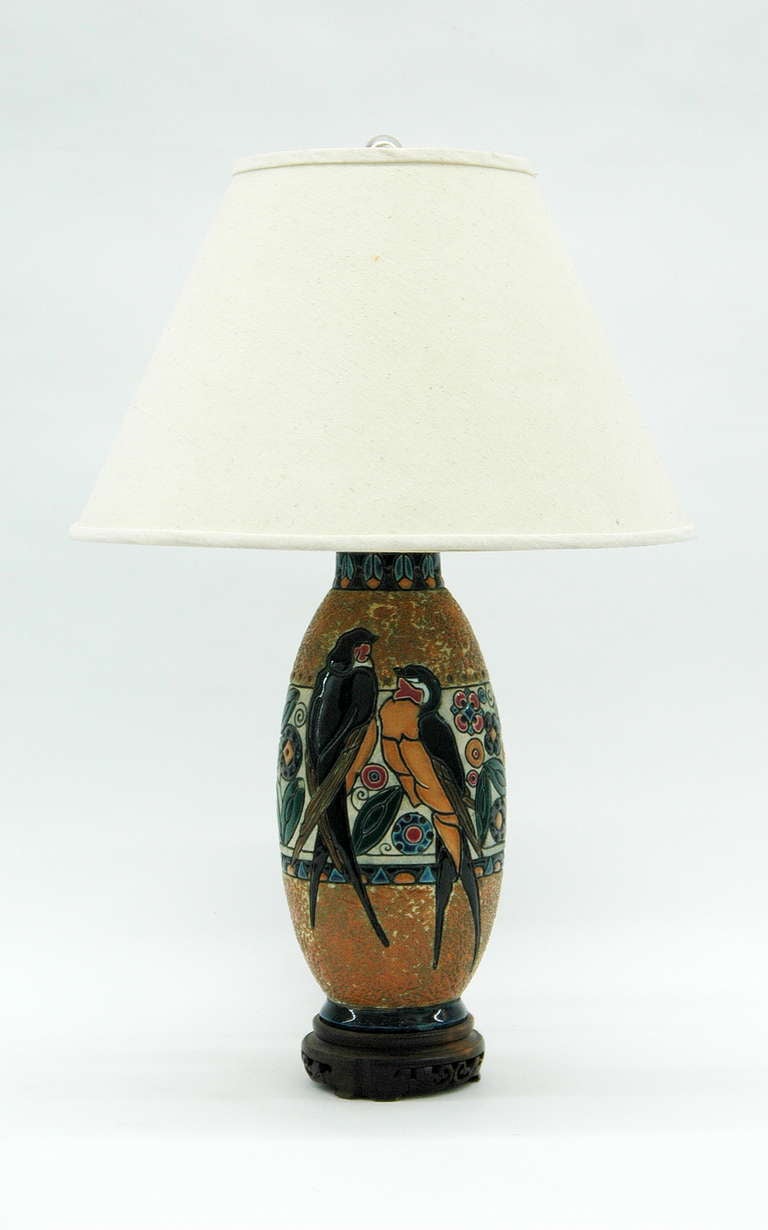 A Table lamp made from a Dutch Gouda pottery Vase decorated with birds and floral patterns. The ceramic body is topped with a brass neck holding two light sockets and finished with a carved wooden base. Lampshade is not included.