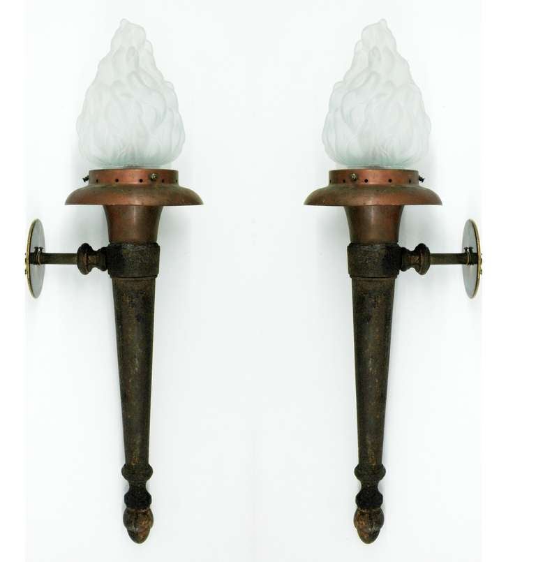 Two sconces in the shape of torches with glass shades resembling fire. The body has some corrosion which suggest the pieces were used outdoors but also enhances the look of antique torches converted from gas lanterns.