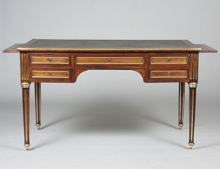 A Louis XVI Neoclassical style brass-mounted writing desk with an inset green leather top, each end of the desk featuring a sliding extension for additional surface space.

The solid fruitwood body accented by mounts and hardware in polished