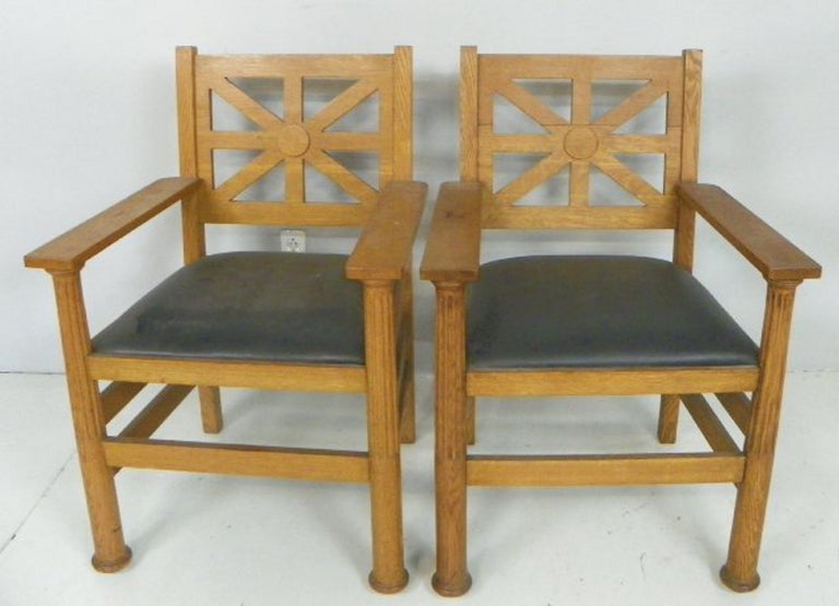 A pair of well-proportioned Arts & Crafts period arm chairs, each chair in solid oak with upholstered leather seat. 

The frames with strong, clean lines accented by touches of neoclassical design in the columnar arm supports and pierced seat back