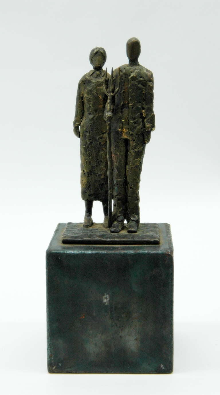 A hammered metal sculpture of the famous painting 'American Gothic' by Grant Wood. The farmer and his daughter are made with similar features of the painting, such as hair and clothing, and placed on a square pedestal of the same material.