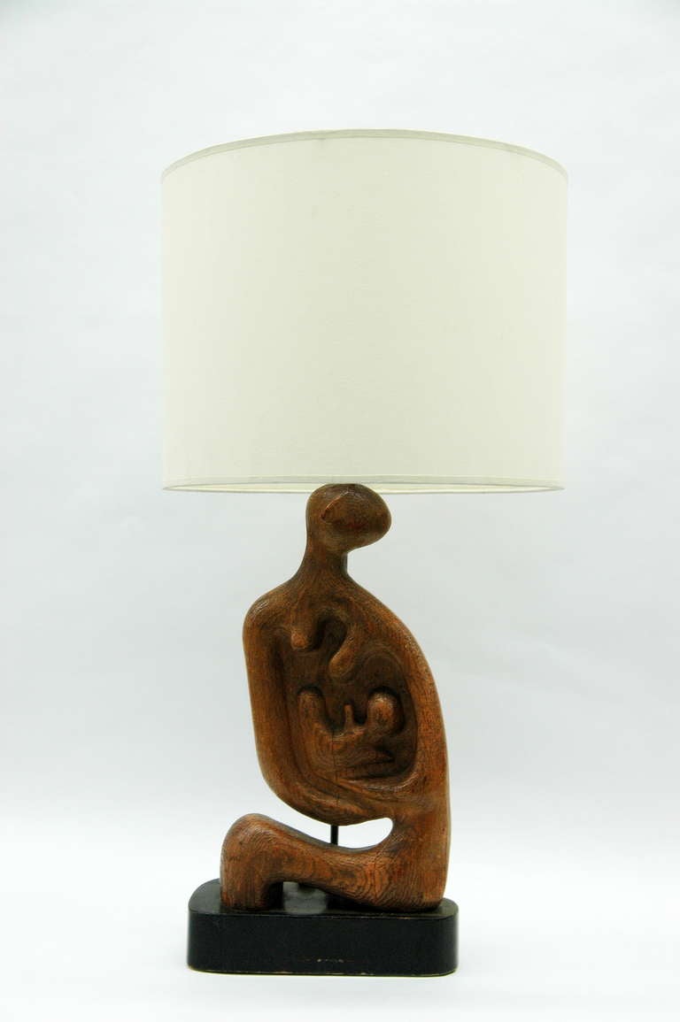 A mid century lamp with a sculpted wood base in the manner of Henry Moore of a theme of mother and child the artist gravitated towards,