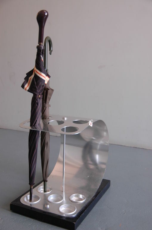 A unique cantilevered umbrella stand formed by a curved plate of chromed metal on a black painted base.