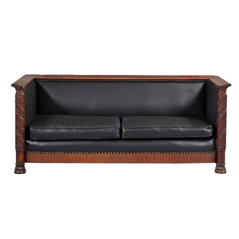 American Classical Revival Mahogany sofa, ca. 1900, of box form with acanthus-carved pilasters at each end above paw feet, covered in faux black leather with brass tack border.

Generous depth and good proportions.