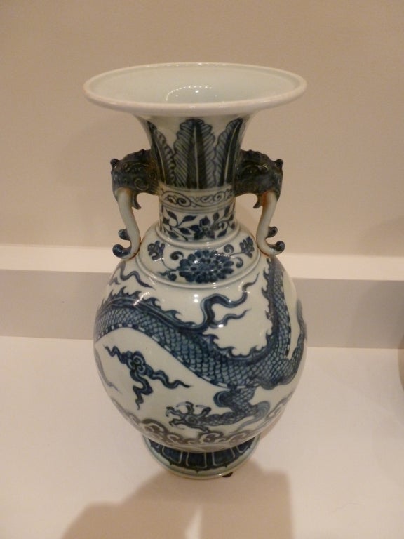 A Tall vase with a depiction of a dragon in the body with stylized leaves on the neck with handles on the neck in the shape of elephants.