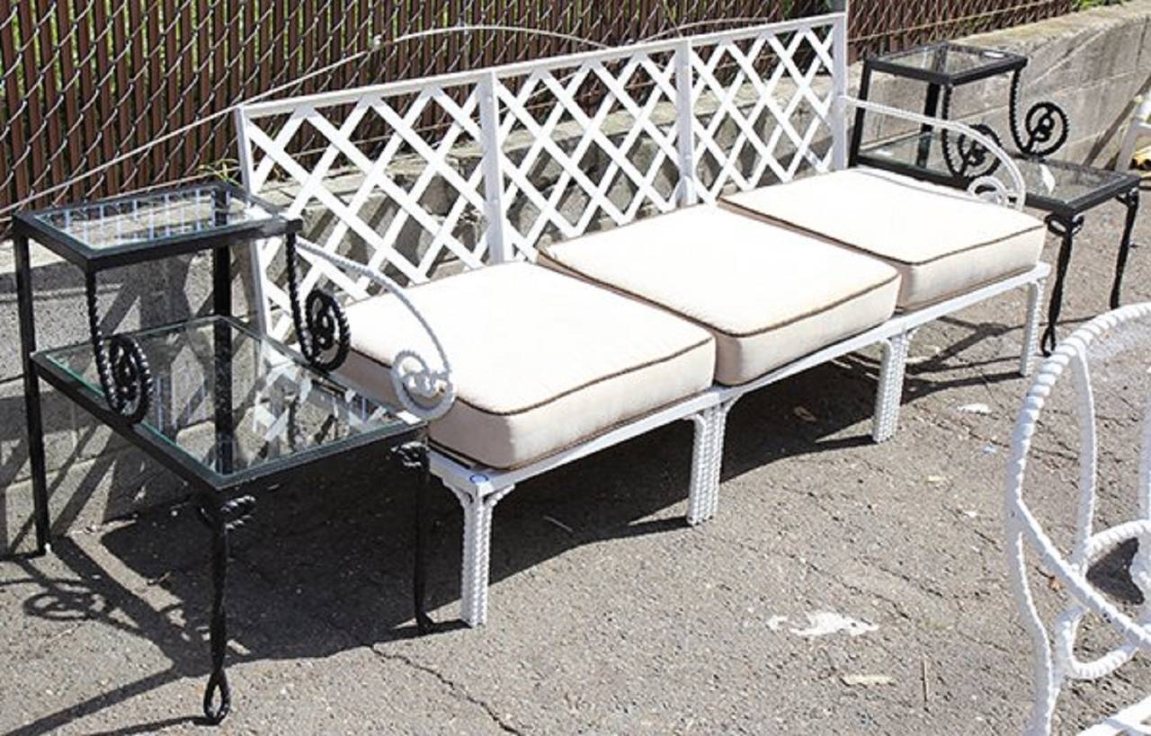 A Classic set of wrought iron patio furniture, each piece having rope turned arms and legs. The set consisting of a three seat sofa, a pair of lounge chairs and side tables with inset glass tops; together with a pair of French bistro style