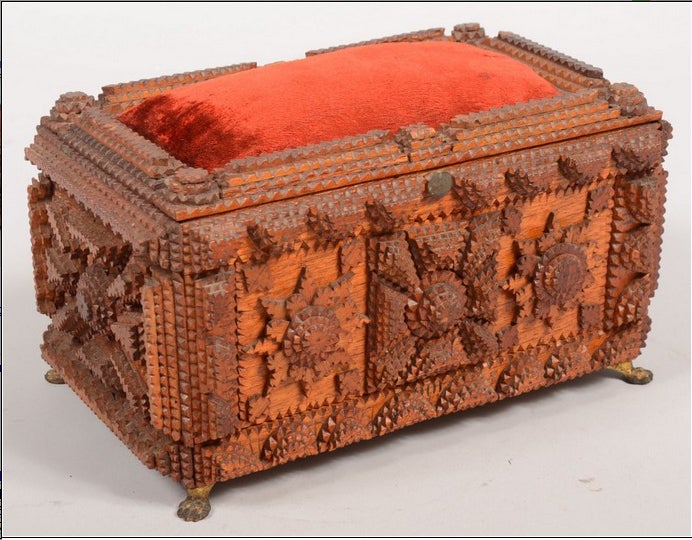 A handcrafted dresser or jewelry box with hinged pincushion lid and applied, chip-carved decoration. The interior with framed mirror on underside of lid and papered in a purple and white printed pattern. The box rests on four cast brass lion paw