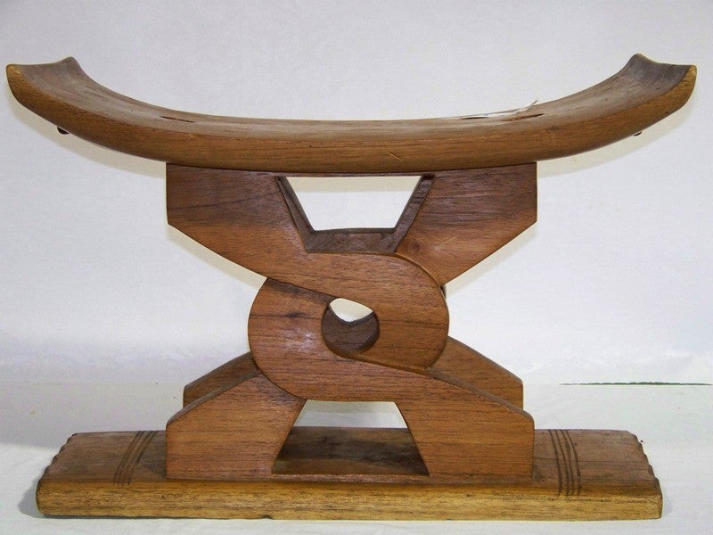 Carved, curved wooden stool with support in an interlocking 'X' pattern on a shallow plinth.
