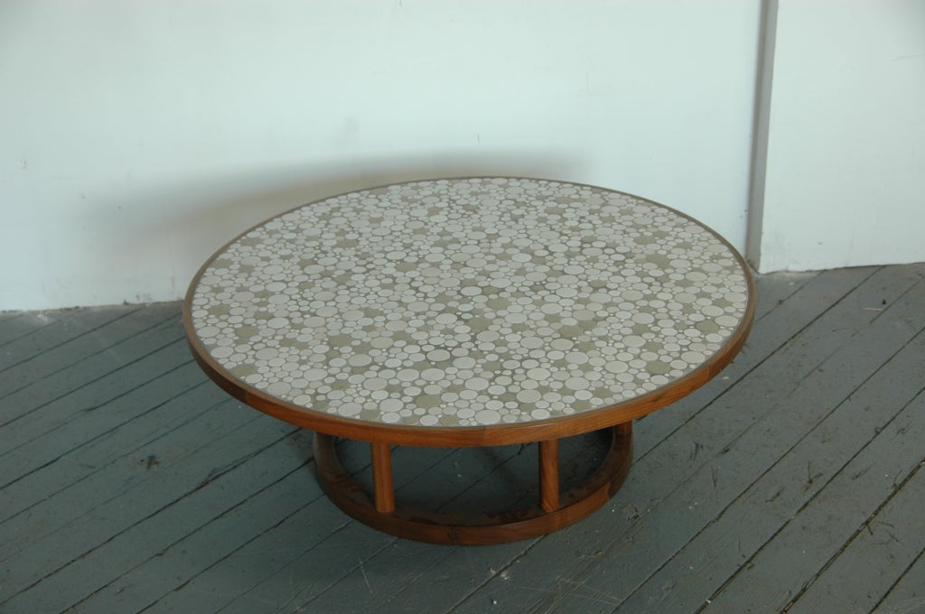 Gorgeous circular coffee table, solid wood frame with tile mosaic top. The top with hundreds of sepia-tone circular tiles in various sizes contained within a wooden edge. Resting atop six cylindrical wood columns on a ring base.

References: A