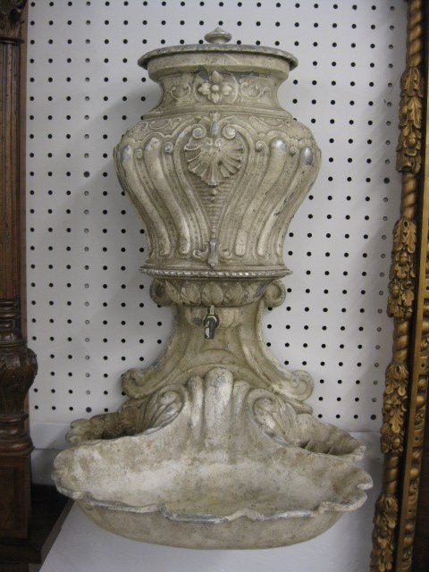 A highly decorated garden wall fountain or sink compromised of a reservoir over a shell sink. Traditionally found in gardens to wash ones hands they are also used decoratively in a powder room with a plant as they are the ancestor of the modern day