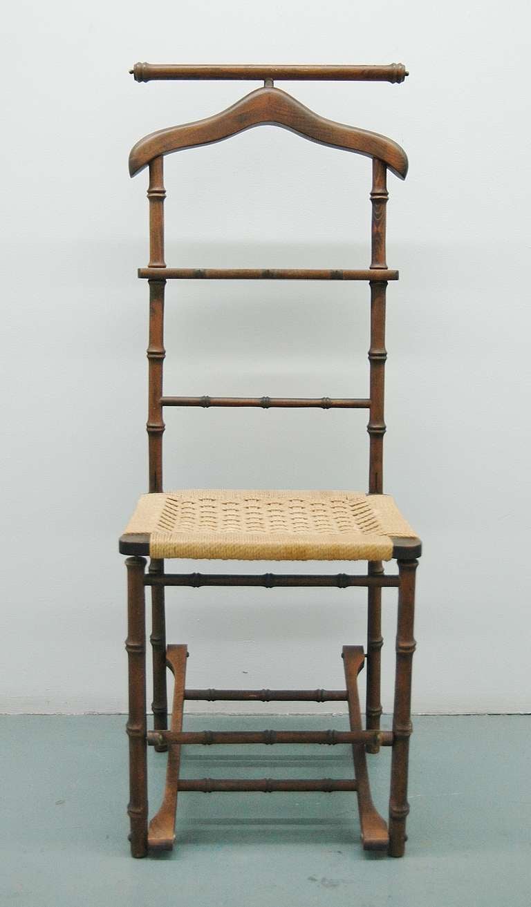 A folding valet chair with a woven rope seat in the Italian tradition with wood carved to mimic rattan or bamboo.