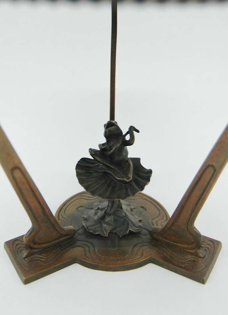 An Austrian Art and Crafts/Art Nouveau Copper table lamp with a hand hammered shade raised by three supports. The shade has three green stone embelishments. A frog resting on a shell playing the guitar sits at the center below the light bulb.