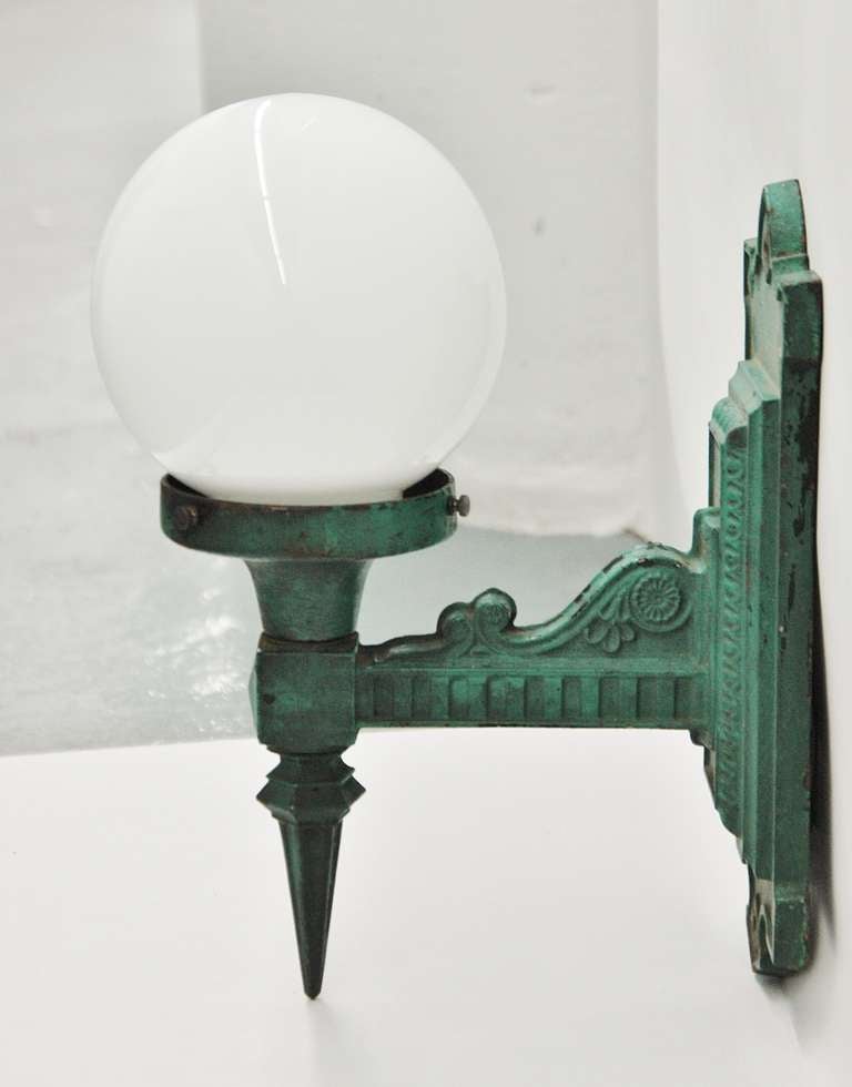 A pair of green painted cast iron wall mount light fixtures with white glass globes. Each piece is labeled 27 and has a 