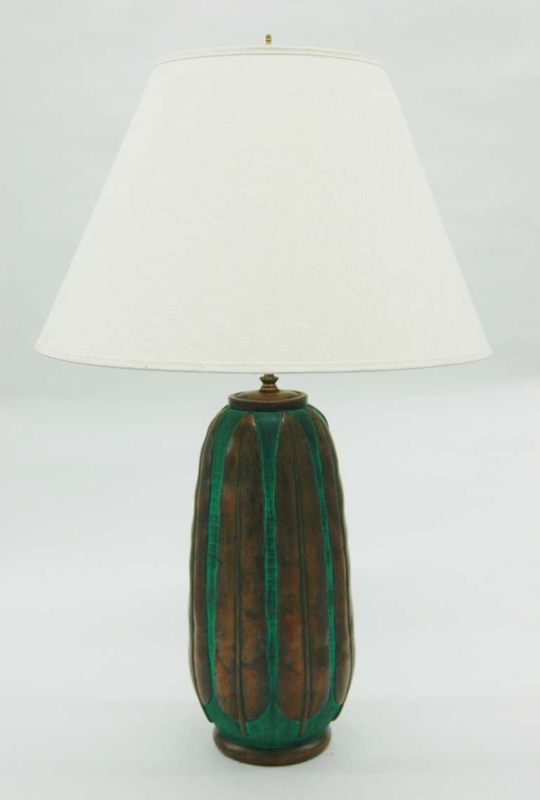 A large lamp with elongated body showing long bronze finished leaves running vertically on the green ground.