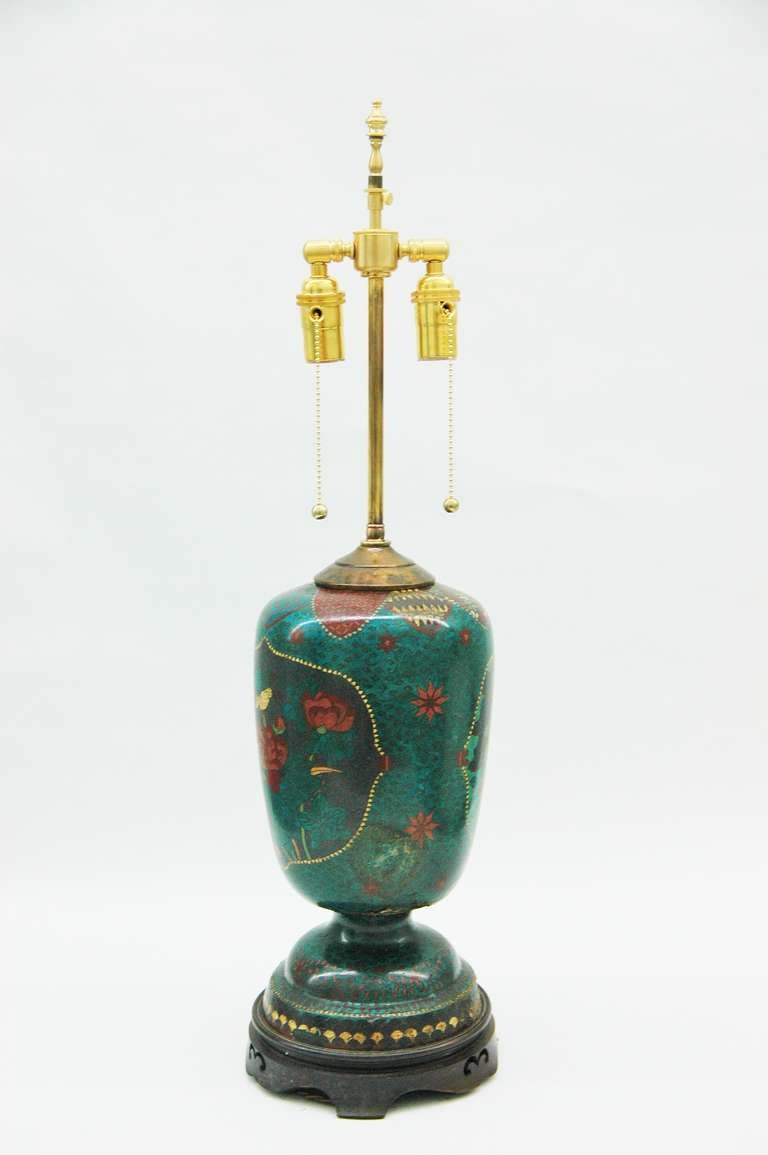 An intricately decorated navy blue and turquoise table lamp with birds and flowers illustrations done in cloisonné on a circular stepped pedestal base on a carved and turned teak wood base. 

The footed jar is 17